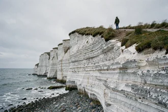 Falaises de craie blanche d'Ault vues depuis le bas, sentier côtier et randonneur en anorak vert au sommet